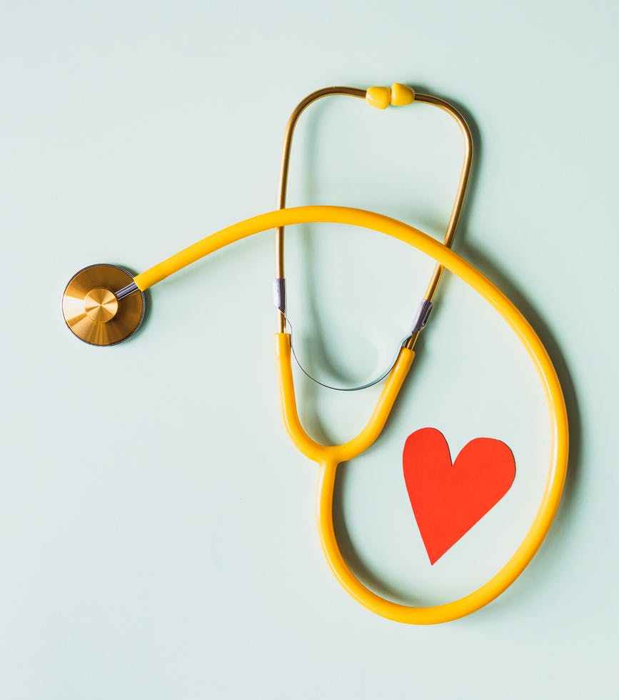 medical stethoscope with red paper heart on white surface