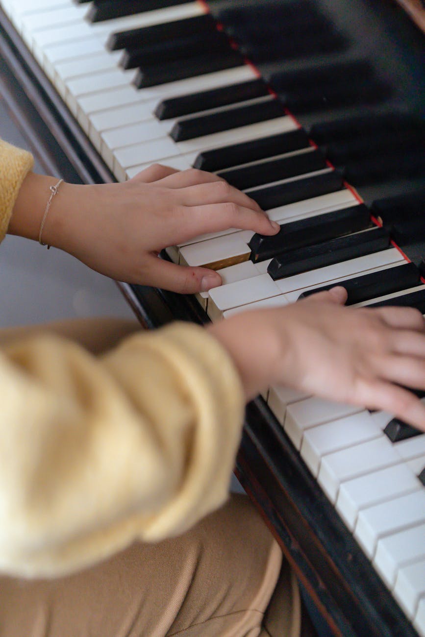unrecognizable female musician playing melody on piano in room